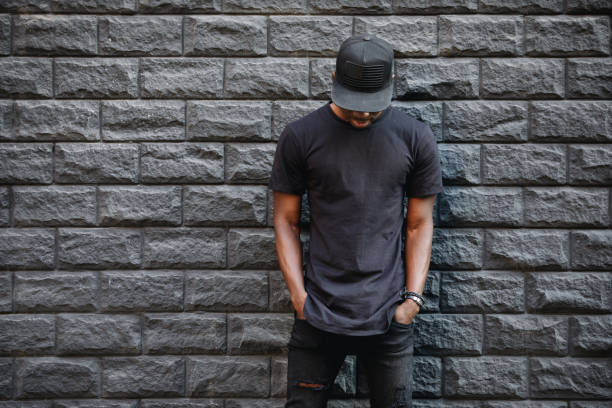 Handsome african american man in blank black t-shirt standing against brick wall