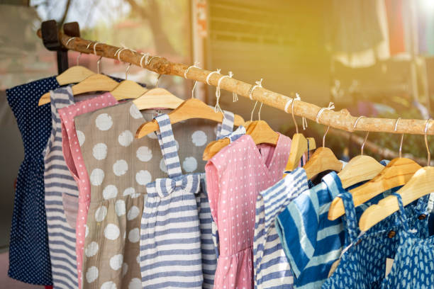 Kids's fashion, cute little girl dress hanging on wooden stick over blurred cloth shop background