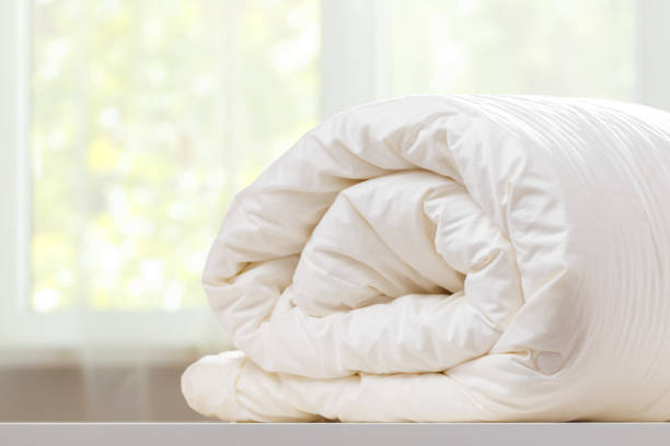 A folded rolls duvet is lying on the dresser against the background of a blurred window. Household.