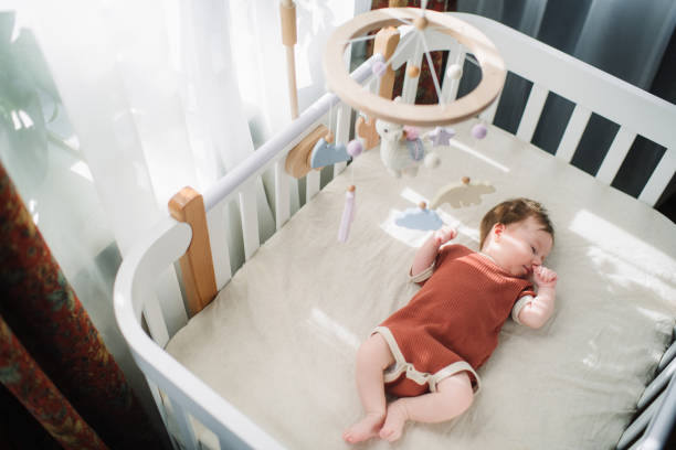 Newborn girl lies in white cradle with mobile above