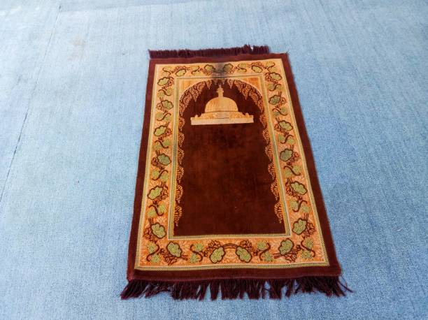 An orange prayer mat with a mosque building motif on a blue carpet