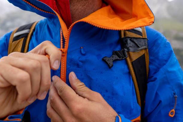 A close-up of a man zipping up his bright blue hiking jacket, emphasizing outdoor adventure gear.