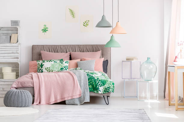 White and pink bedroom interior with leaves drawings hanging above a cozy bed with knit blankets